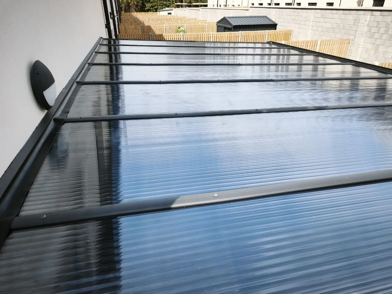 Fixed polycarbonate roof on a wall-mounted aluminium pergola