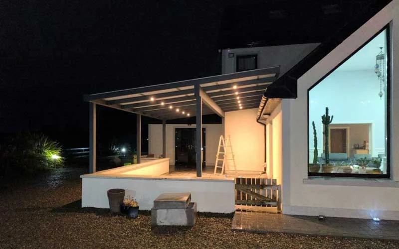 Wall-mounted pergola with trapezoidal roof and integrated LED lighting