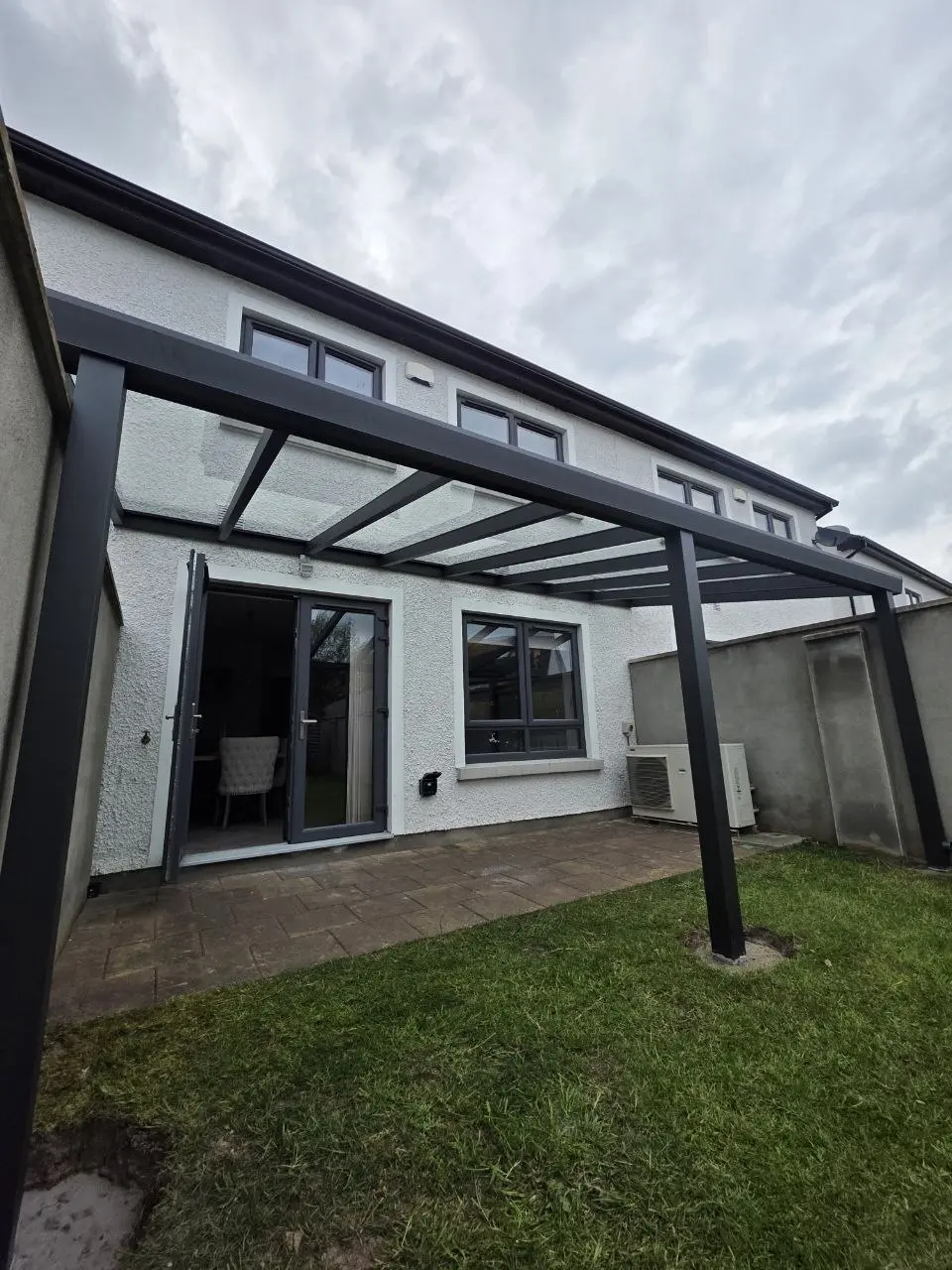 Wide garden view of the completed wall-mounted glass pergola in Leixlip