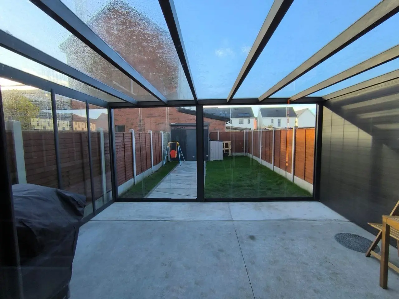Safety glass roof and black aluminium rafters viewed from inside the pergola