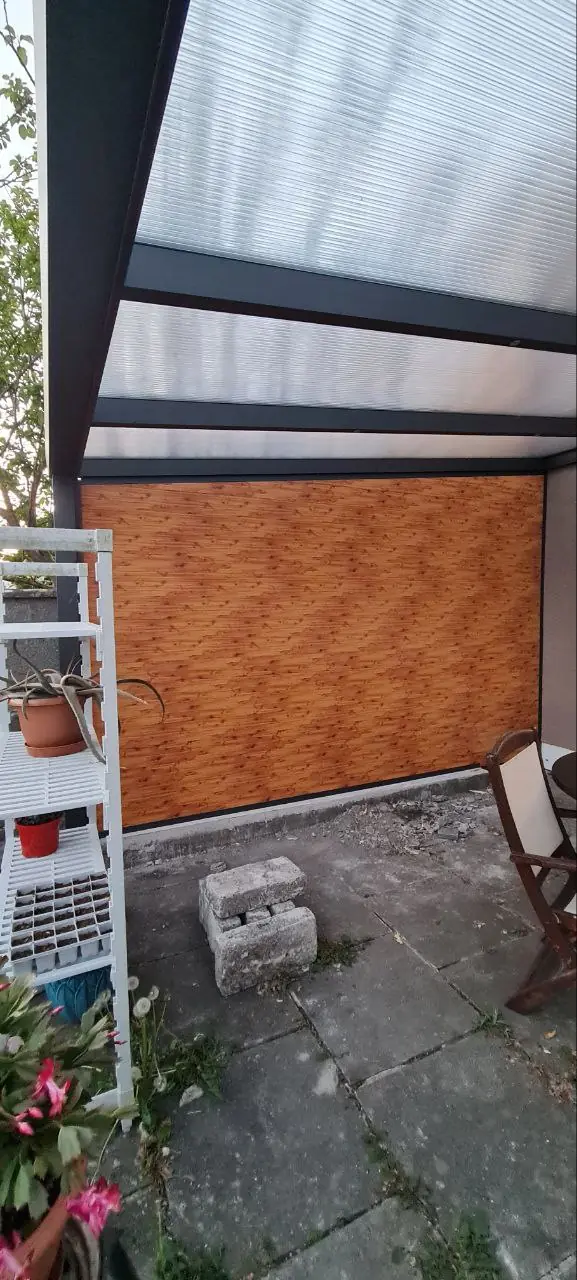 Wood-effect tongue-and-groove side wall beneath the completed polycarbonate pergola roof